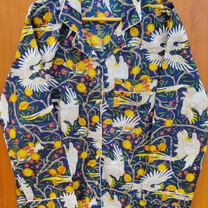 May include: A blue long-sleeved shirt with a white button-up collar. The shirt has a white and yellow floral pattern with white birds.