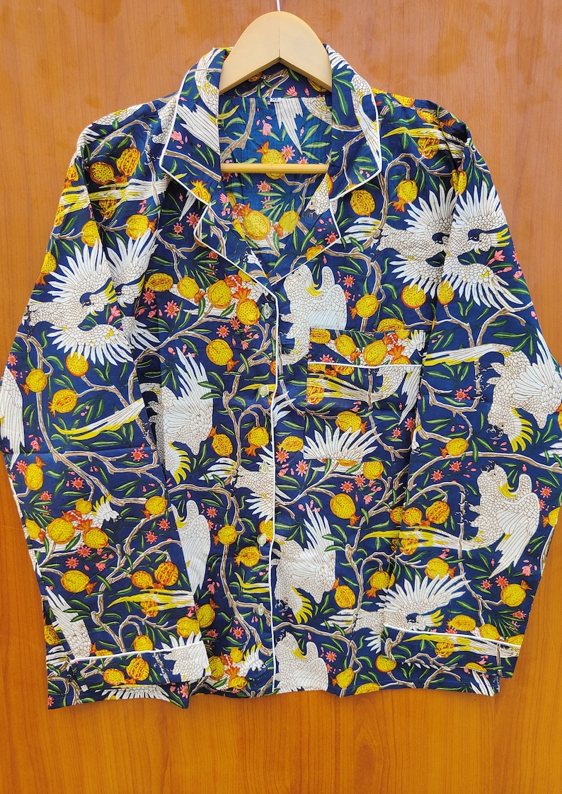May include: A blue long-sleeved shirt with a white button-up collar. The shirt has a white and yellow floral pattern with white birds.