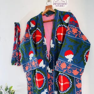 May include: A long, blue cotton robe with a red and white floral embroidery pattern. The robe has a red and white striped lining and a matching tie belt.