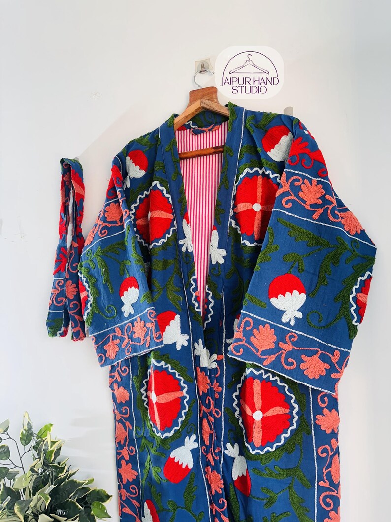 May include: A long, blue cotton robe with a red and white floral embroidery pattern. The robe has a red and white striped lining and a matching tie belt.