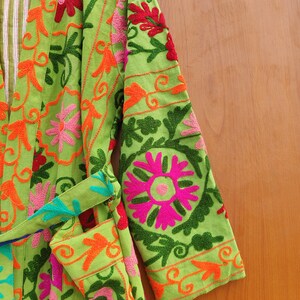 May include: A green robe with colourful floral embroidery. The robe has a tie belt and long sleeves.