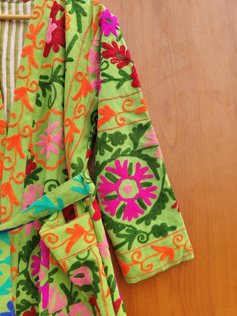 May include: A green robe with colourful floral embroidery. The robe has a tie belt and long sleeves.