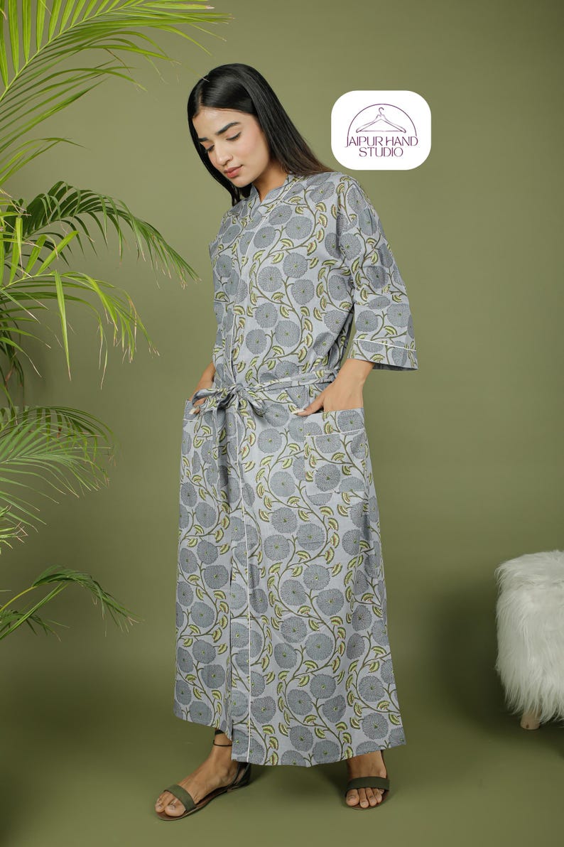 Puede incluir: Una bata gris con estampado floral, ribete blanco y lazo a juego. La bata tiene mangas tres cuartos y bolsillos. El logotipo de Jaipur Hand Studio est&aacute; en la esquina superior derecha.