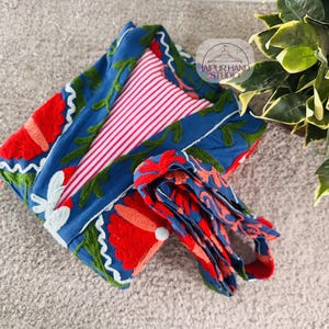 May include: A blue and red floral embroidered robe with a pink and white striped lining. The robe is folded and tied with a matching blue and red floral embroidered sash. The text "Jaipur Hand Studio" is visible on a tag.