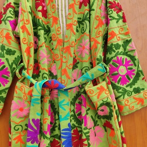 May include: A green robe with colourful floral embroidery. The robe has a tie belt and long sleeves.