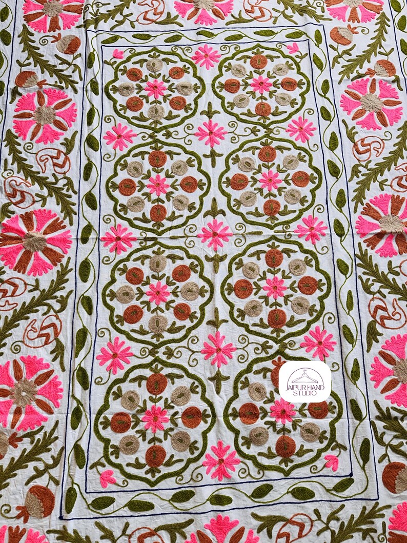 May include: White cotton throw blanket with intricate embroidery in shades of pink, brown, and green. The design features repeating floral motifs and a central logo that reads "Jaipur Hand Studio".