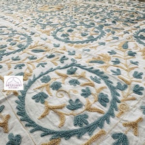 Peut inclure: Tissu de coton blanc avec une broderie complexe en bleu sarcelle et beige. Le motif présente un motif répétitif de motifs floraux stylisés.