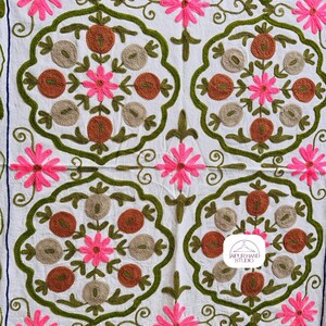 May include: White fabric with a repeating pattern of green, brown, and pink embroidered flowers. The fabric has the text "JAIPUR HAND STUDIO" in a white circle with a hanger icon.