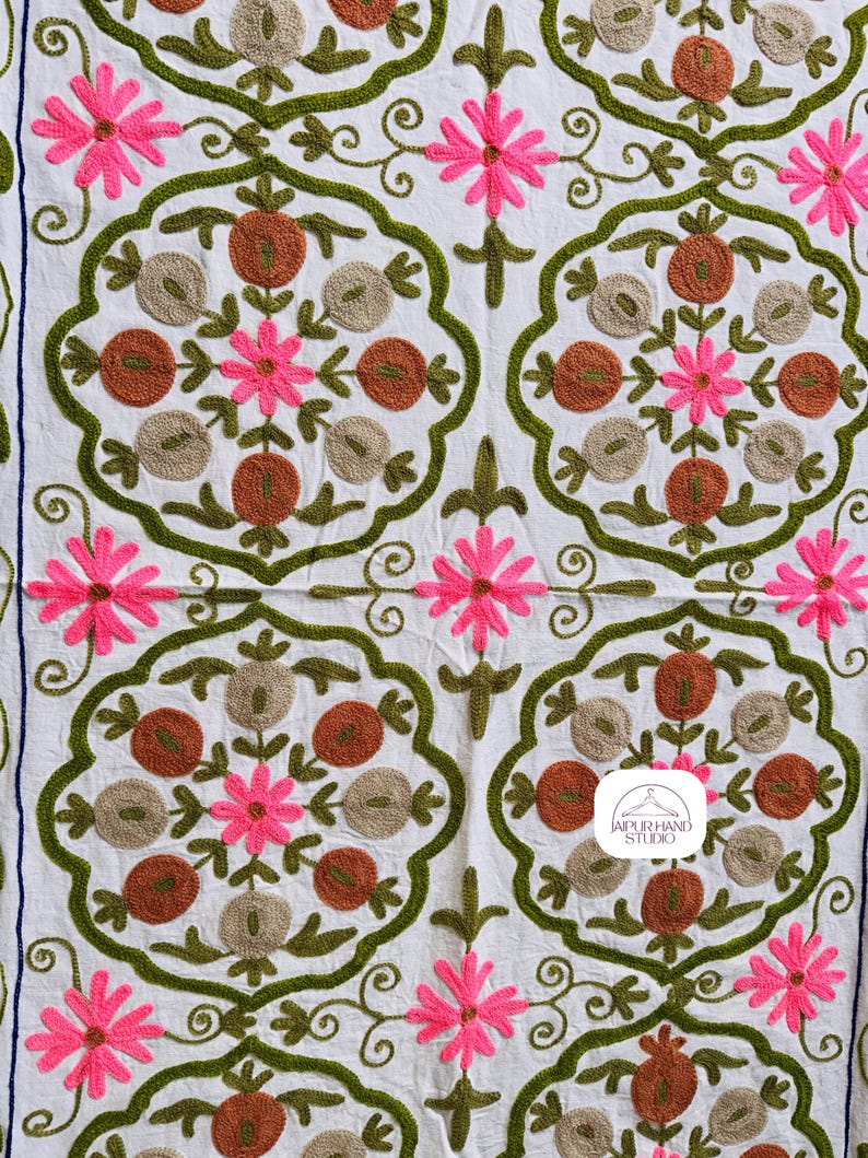 May include: White fabric with a repeating pattern of green, brown, and pink embroidered flowers. The fabric has the text "JAIPUR HAND STUDIO" in a white circle with a hanger icon.
