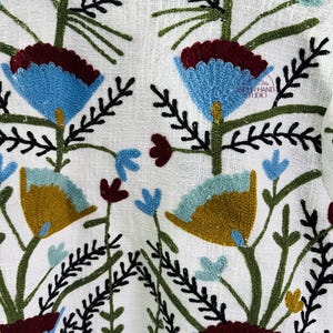 Puede incluir: Chaqueta de lino blanca con dise&ntilde;os florales bordados de colores. El bordado presenta flores azules, verdes, amarillas y rojas.