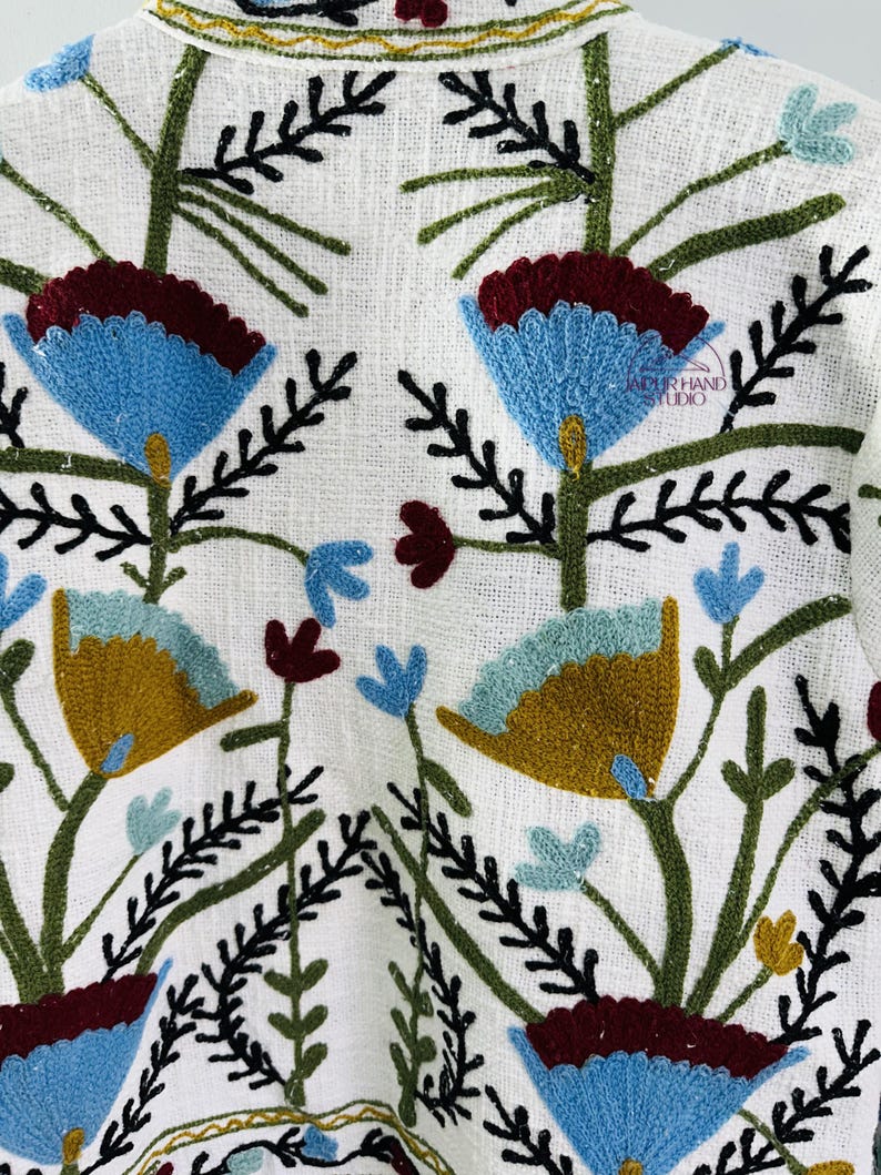 Puede incluir: Chaqueta de lino blanca con dise&ntilde;os florales bordados de colores. El bordado presenta flores azules, verdes, amarillas y rojas.