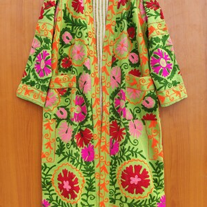 May include: A long green embroidered jacket with floral patterns in shades of pink, red, and orange. The jacket has a striped lining and two pockets.