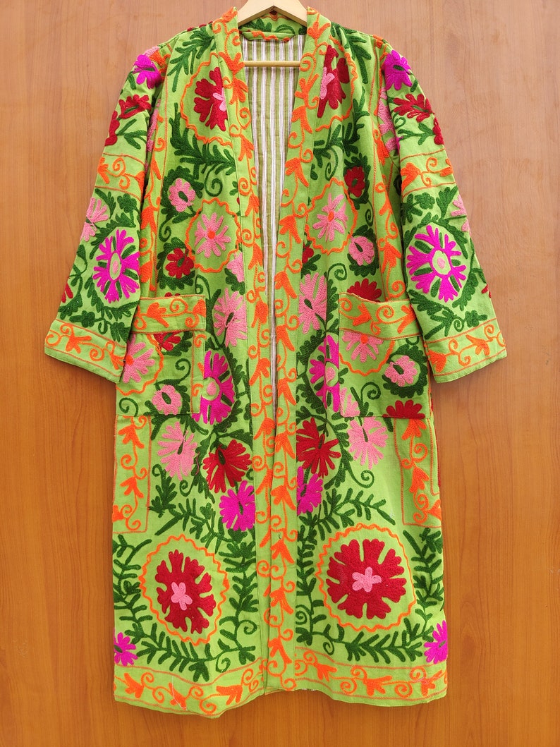 May include: A long green embroidered jacket with floral patterns in shades of pink, red, and orange. The jacket has a striped lining and two pockets.