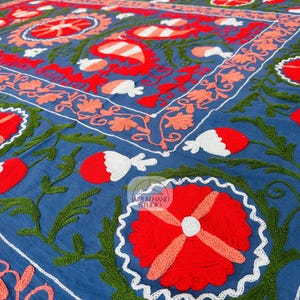 May include: A blue cotton fabric with intricate hand embroidery in red, white, and green. The design features floral motifs and paisley patterns.
