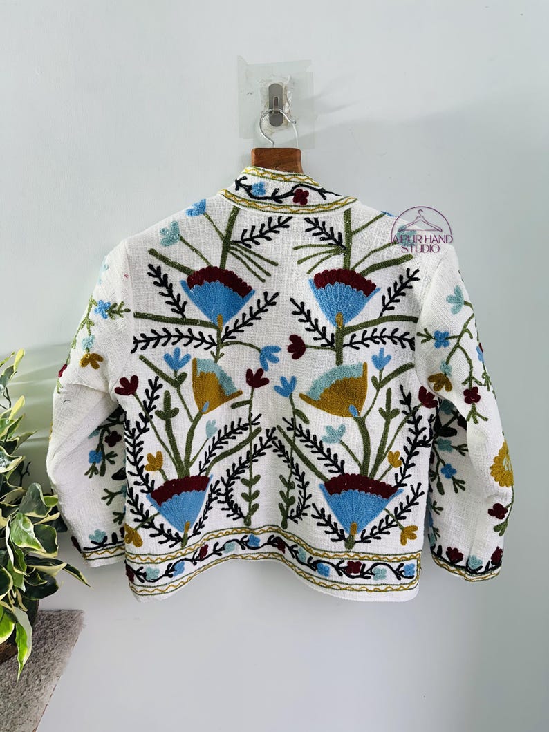 Puede incluir: Chaqueta de lino blanca con bordado floral de colores. El bordado presenta flores azules, rojas, verdes y amarillas.
