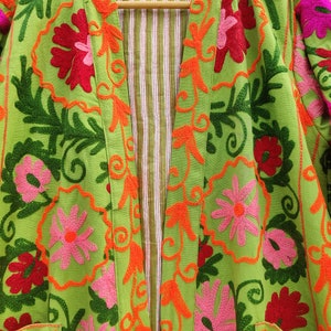 May include: A green cotton jacket with colourful floral embroidery. The jacket has a long sleeve and a front opening with a striped lining.