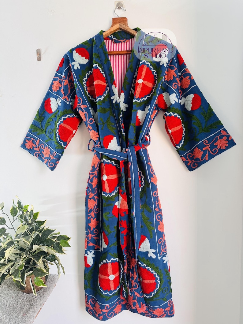 May include: A blue cotton robe with a floral embroidery design. The robe has a red, white, and green floral pattern. The robe has a tie belt and a red and white striped lining.