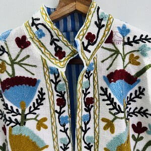 Puede incluir: Chaqueta blanca bordada con forro a rayas azul y blanco. El bordado presenta dise&ntilde;os florales en tonos azules, verdes, rojos y amarillos.