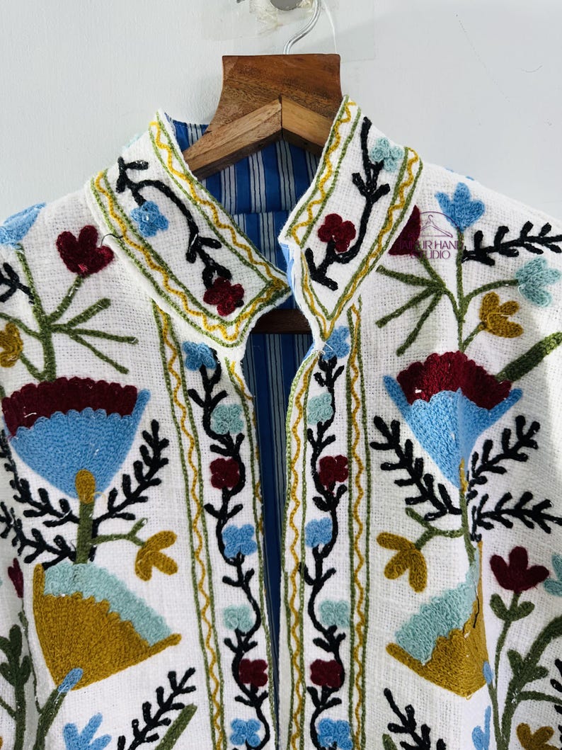 Puede incluir: Chaqueta blanca bordada con forro a rayas azul y blanco. El bordado presenta dise&ntilde;os florales en tonos azules, verdes, rojos y amarillos.