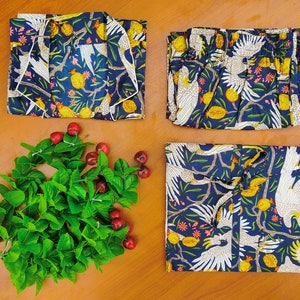 May include: Three pieces of blue and white patterned fabric with a design of white birds and yellow fruit. The fabric is folded and arranged on a wooden surface.