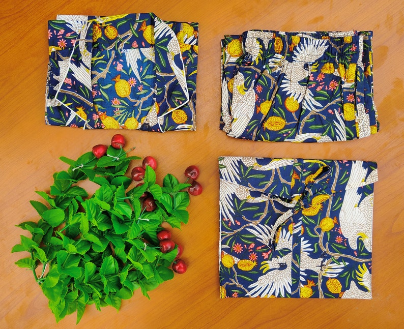 May include: Three pieces of blue and white patterned fabric with a design of white birds and yellow fruit. The fabric is folded and arranged on a wooden surface.