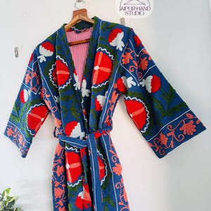 May include: A blue cotton robe with red, white, and green floral embroidery. The robe has a tie belt and long sleeves.