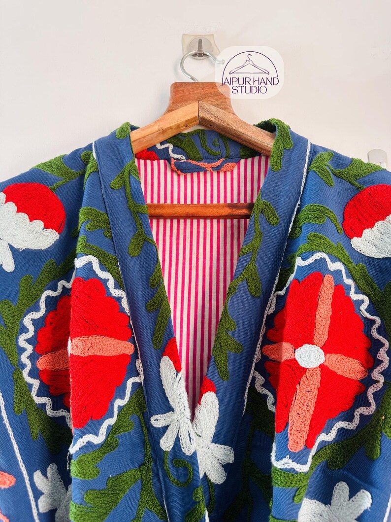 May include: A blue embroidered jacket with a pink and white striped lining. The embroidery features red, white, and green flowers.