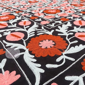Peut inclure: Gros plan sur un textile noir avec une broderie florale complexe. Le motif présente de grandes fleurs orange et roses avec des feuilles et des tiges blanches et bleu clair. La broderie est détaillée et vibrante.