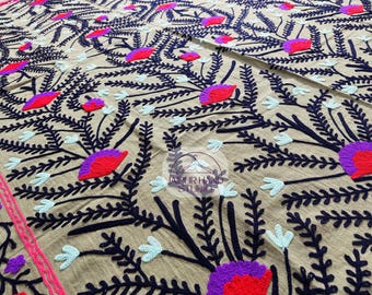 Pode incluir: Tecido bege com um design de bordado floral. As flores são vermelhas, roxas e azuis, e as folhas são pretas. O tecido tem uma sensação leve e arejada.