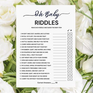 May include: A white baby shower game card with the words "Oh Baby Riddles" in elegant script. The card features a list of riddles with checkboxes for answers, surrounded by white flowers.