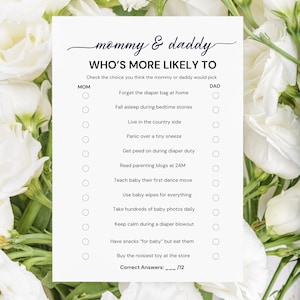 May include: A white paper game card with the text "mommy & daddy WHO'S MORE LIKELY TO". The card lists questions about parenting, with spaces to check for mom or dad. The card is surrounded by white flowers.