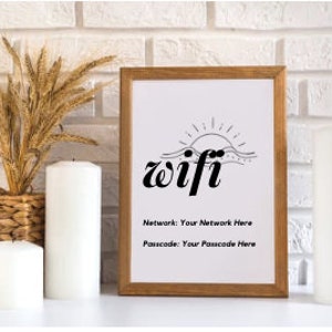 Puede incluir: Una impresión enmarcada con una ilustración en blanco y negro de un sol poniéndose sobre las olas. El texto "wifi" está escrito en una fuente en negrita y estilizada. Debajo de la ilustración, el texto "Red: Tu red aquí" y "Contraseña: Tu contraseña aquí" está impreso en negro.