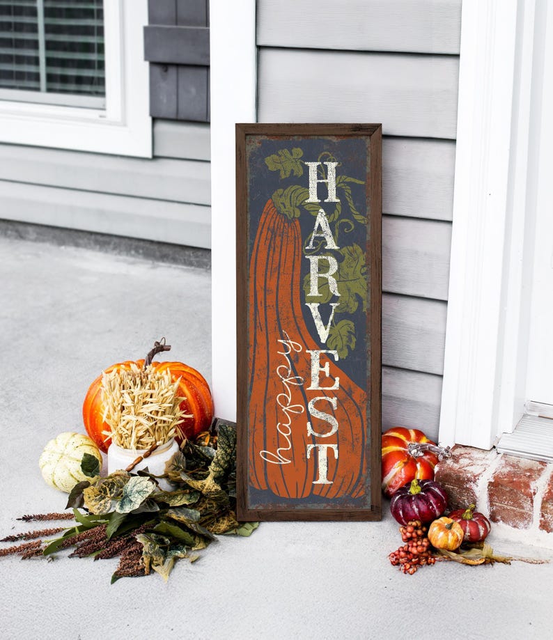 Tall harvest sign in navy leaning on white siding with pumpkins and a harvest bouquet.
