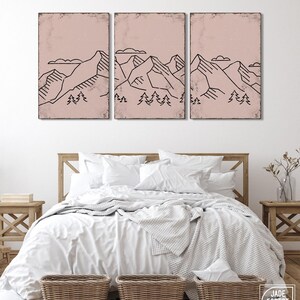 May include: A triptych of framed art prints featuring minimalist black line drawings of mountain ranges and trees against a dusty rose background. The artwork is displayed above a bed with white bedding and wicker baskets.