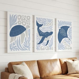 A print set with the sea creature design hangs above a leather sofa with cream pillows and a throw.