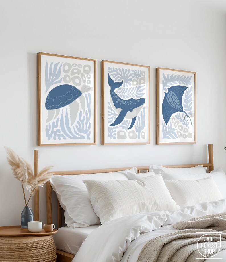 A dusty blue print set of the sea creature design hangs above a wood nightstand and a white bed with a pampas vase.