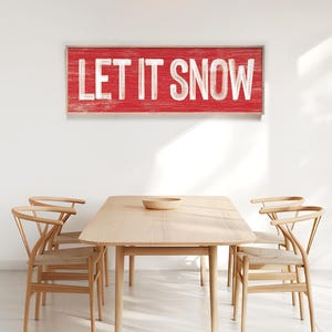 Barn red "Let It Snow" wall print hung above a wood dining table.