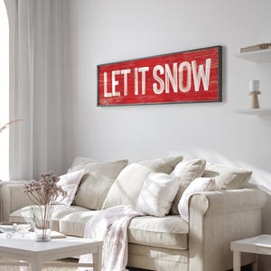 Cozy winter "Let It Snow" sign in barn red hung above a light sofa in a farmhouse living room.