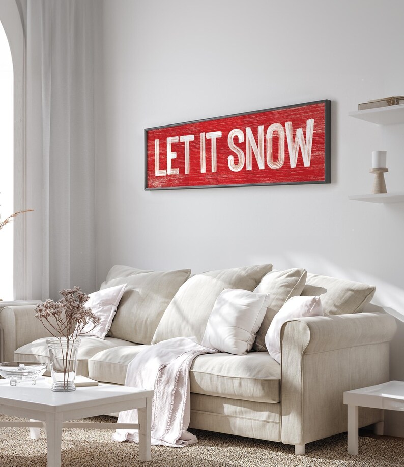 Cozy winter "Let It Snow" sign in barn red hung above a light sofa in a farmhouse living room.