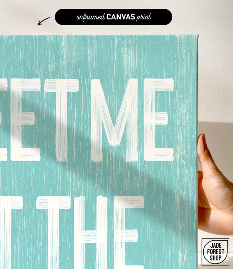A hand touching the corner of the Meet Me At The Beach sign, showing the lettering up close as the unframed canvas print option.