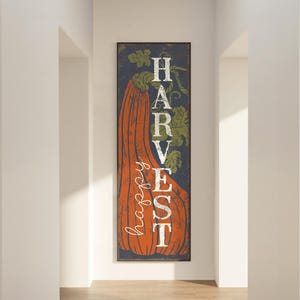 Cream harvest lettering over a large orange pumpkin on navy, seen close against a pale wall.