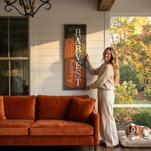 Woman standing beside the navy harvest panel on a porch with a rust orange sofa and a dog.