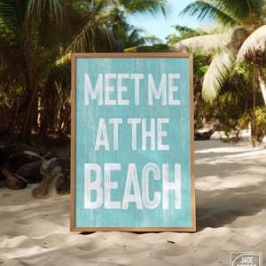 The teal Meet Me At The Beach sign in a wood frame displayed outdoors on a sandy beach near a palm tree.