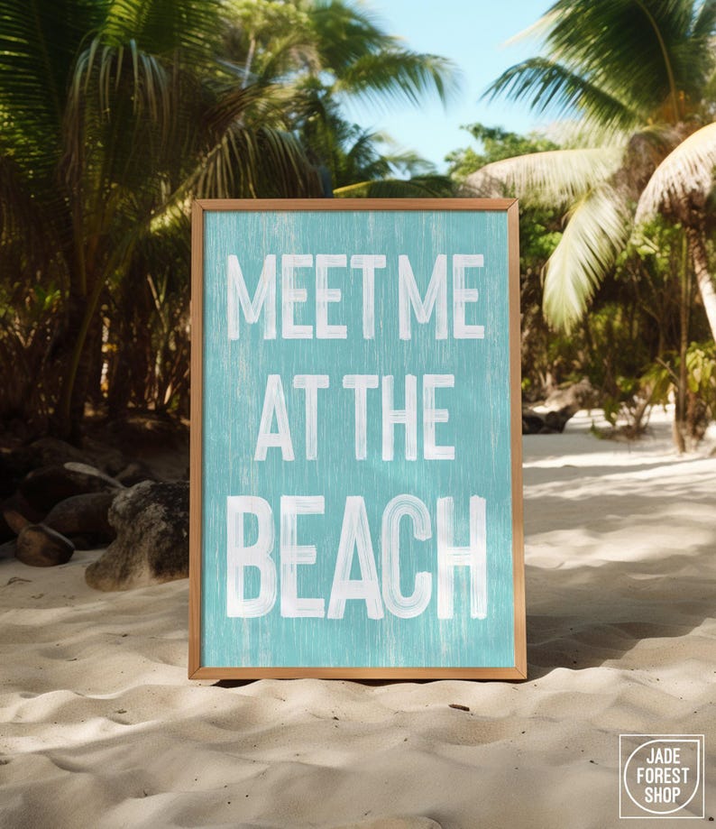 The teal Meet Me At The Beach sign in a wood frame displayed outdoors on a sandy beach near a palm tree.