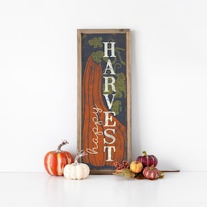 Framed navy harvest panel standing on a white surface among orange and white pumpkins.