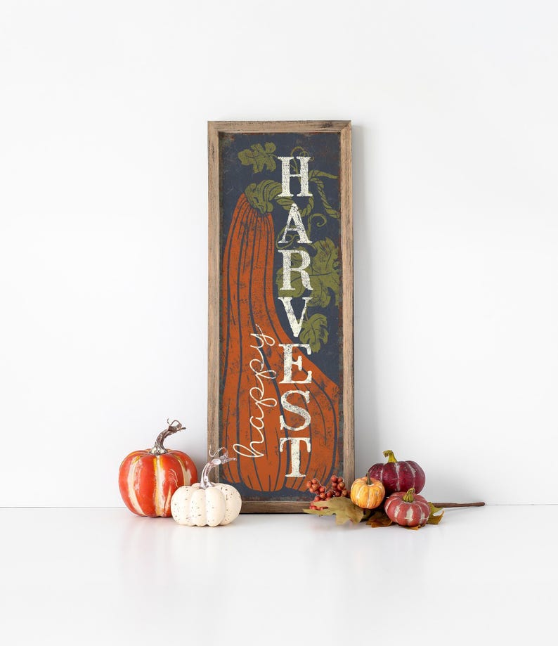 Framed navy harvest panel standing on a white surface among orange and white pumpkins.