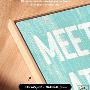 A corner detail of the Meet Me At The Beach sign in a natural wood frame, labeled as the canvas print with natural frame option.