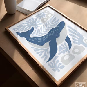 A whale print from the sea creature set rests at an angle in a natural frame on a wood table beside a vase.