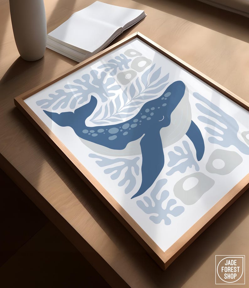 A whale print from the sea creature set rests at an angle in a natural frame on a wood table beside a vase.