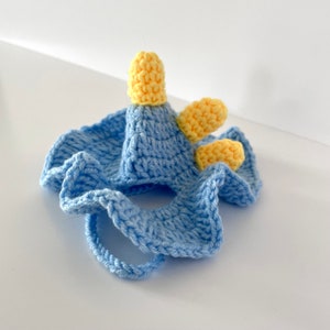 May include: A light blue crocheted pet costume with yellow crocheted horns. The costume has a hole for the pet's head and a strap to secure it.
